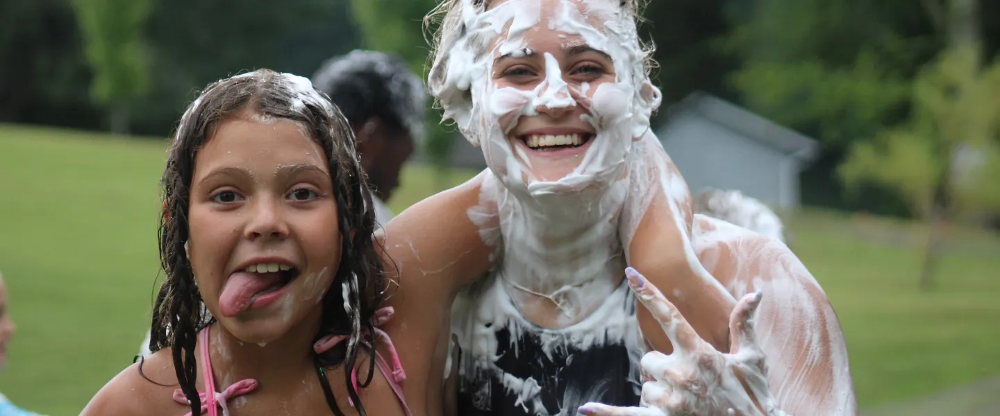 Girl with tong out and another older girl with shaving cream covering her