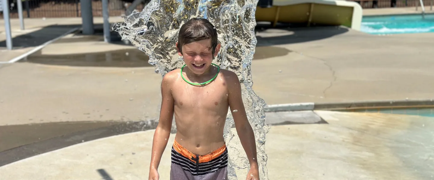 Boy under dump buckets at pool with a smile