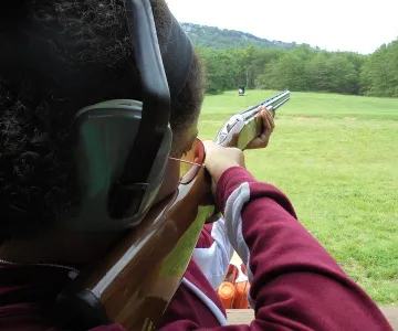 A person looking down the barrel of a shotgun pointed out at 5 stand shot gun field.