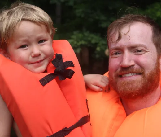 Father holding son while both wearing PFD's about to go down the lake slide.